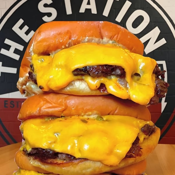 Two stacked Refuel at The Station cheeseburgers with melted cheese and a brioche bun.