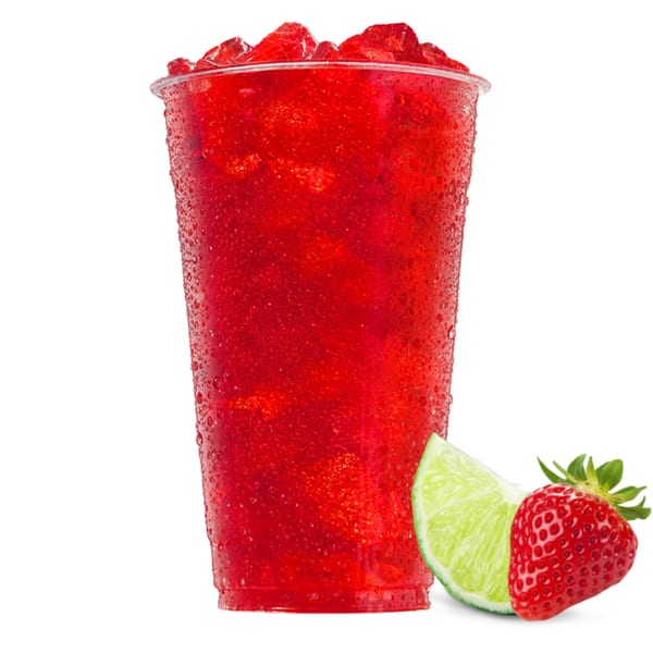 A vibrant red strawberry slushie in a clear cup with a lime wedge and strawberry beside it.